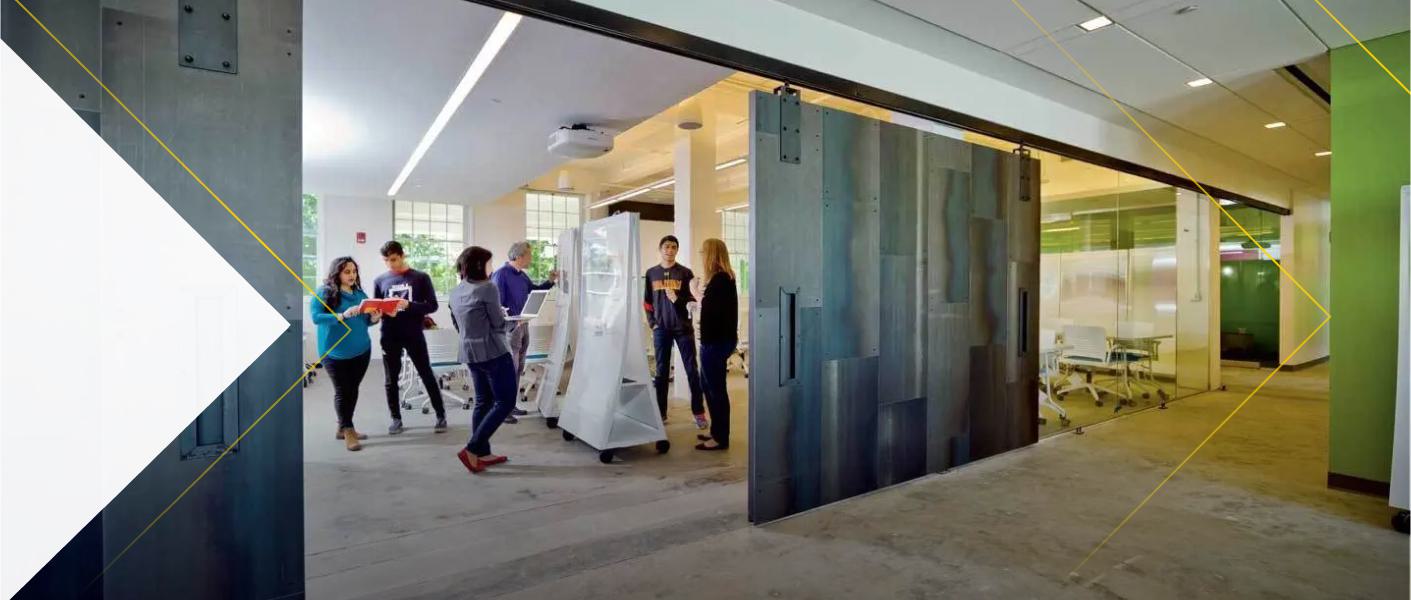 A triangular white graphic overlay frames a photograph of several people collaborating around a mobile whiteboard in a bright, modern office space.
