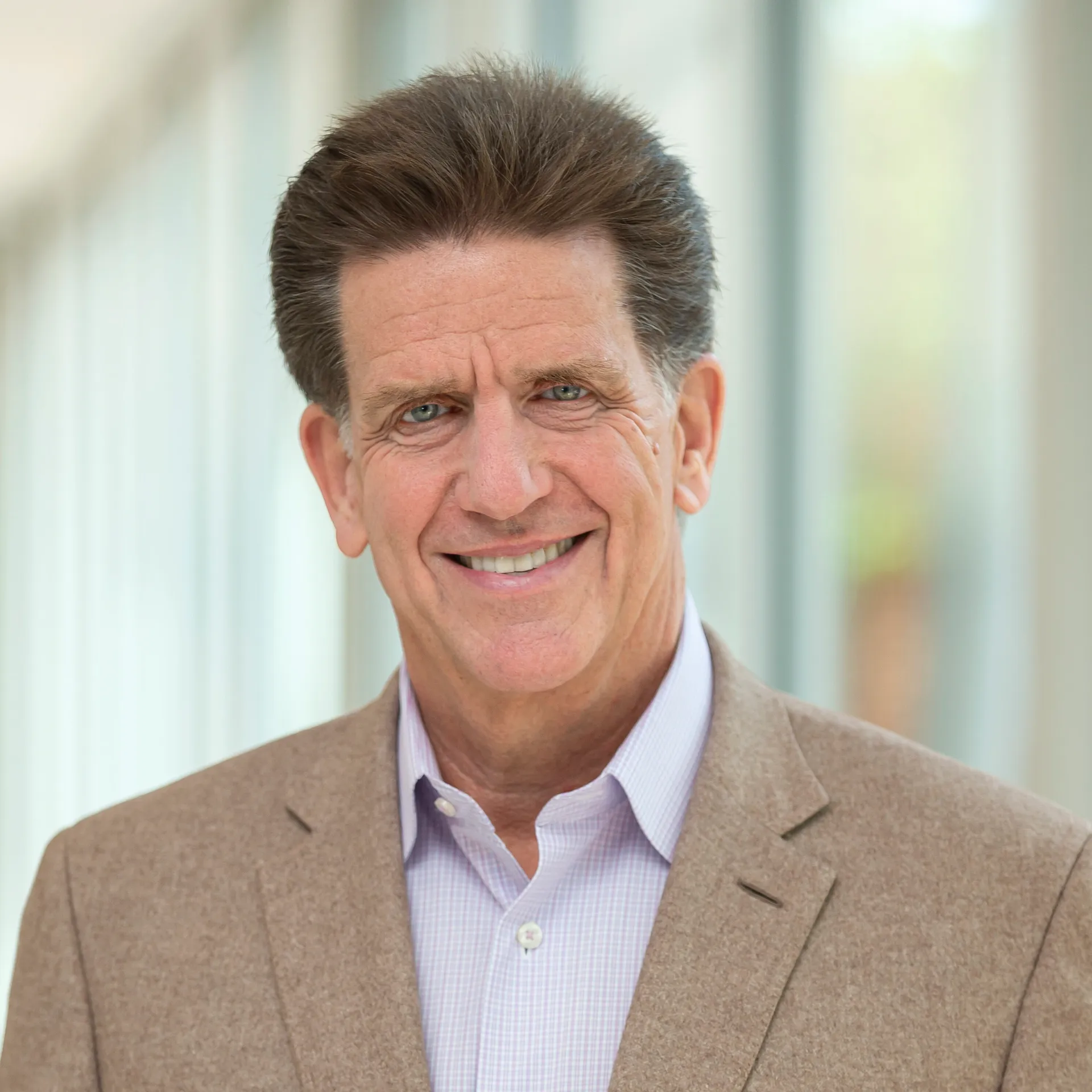 A man wearing a button up shirt and a blazer smiles.