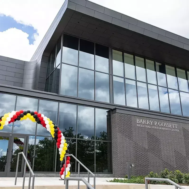 The exterior of a building with gray walls and large windows. A partly cloudy sky is above.