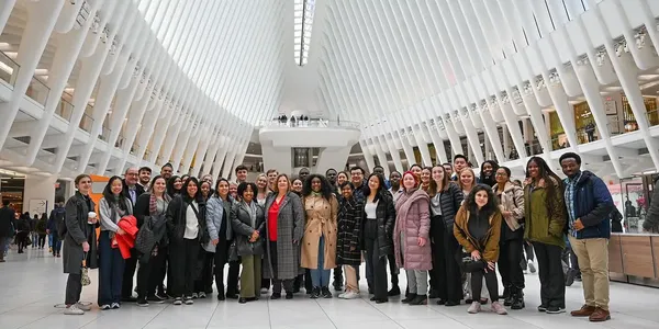 A group of a few dozen people standing together for a photo inside a large room with white features.