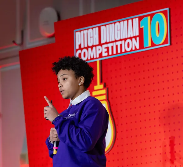 A person holds up a hand with one finger up, a red screen in the background reads, "Pitch Dingman Competition 10."