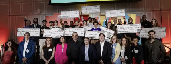 A group of people standing in a ballroom, many of them are students who are holding up large bank checks.