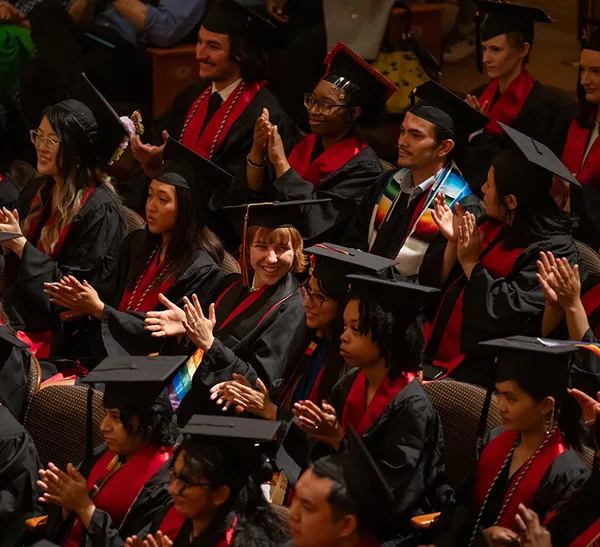 A group of Maryland students dressed in graduation regalia clap.