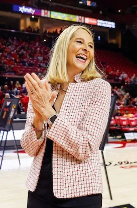 University of Maryland women's basketball coach Brenda Freese smiles and claps while standing on a basketball court.