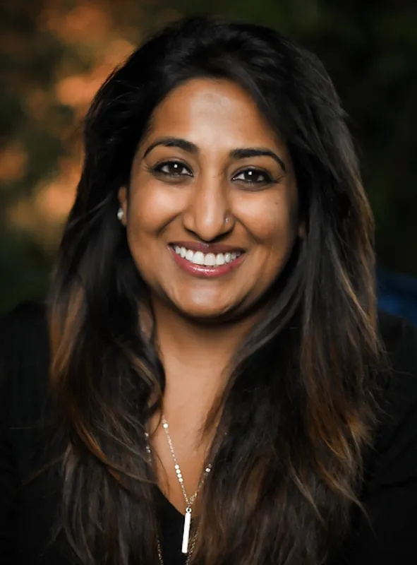 A person with long, brown hair smiles, wearing a black shirttop