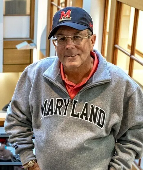 Steve Schanwald is standing next to a railing in an academic building, with his hands in his pockets.