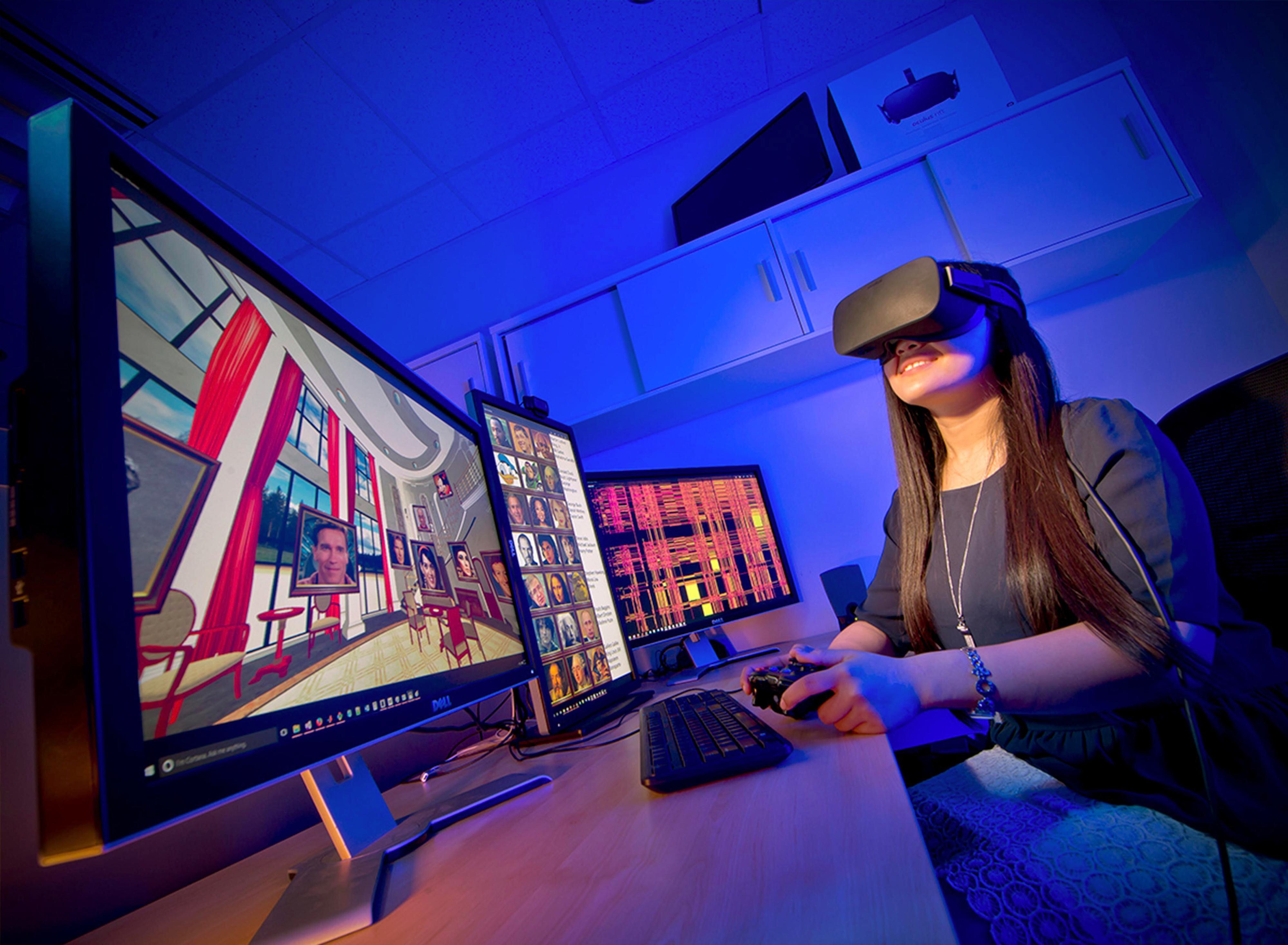 Student in a darkened room working with Virtual Reality technology with monitors