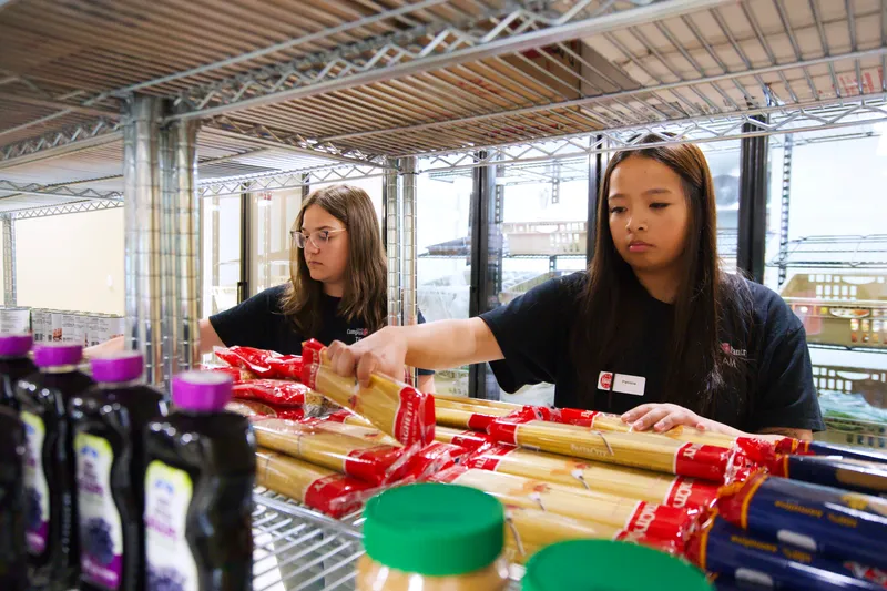 Two people stock items in a pantry.