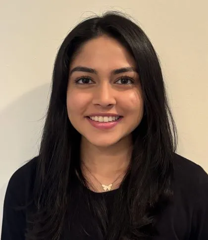A person with shoulder length hair smiles while wearing a black shirt and a necklace.