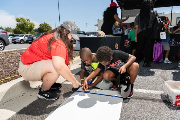 A woman on the left crouches down as two boys next to her use various tools on top of a poster board.