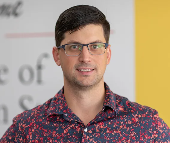 A man wearing glasses and a shirt smiles.