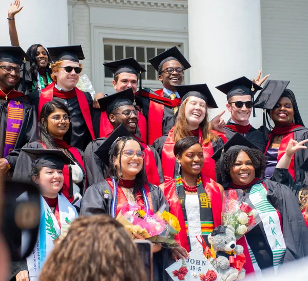 Several students pose for photos while wearing graduation regalia.