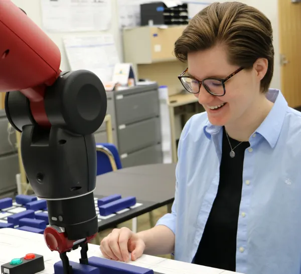 A person smiles while looking at a 3D printer on a table.