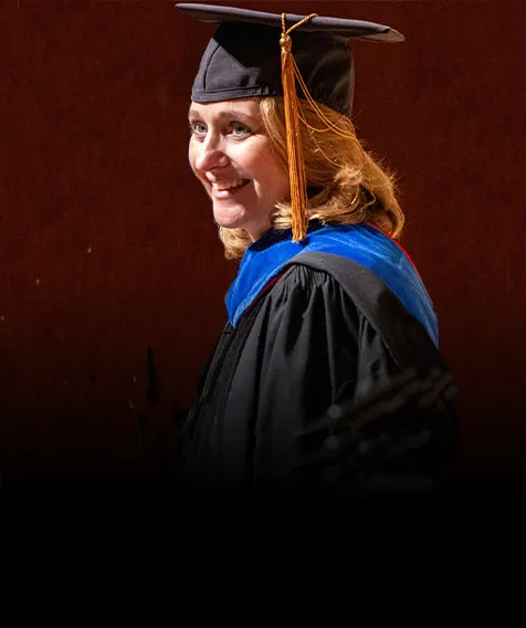 A person wearing graduation cap and gown smiles.