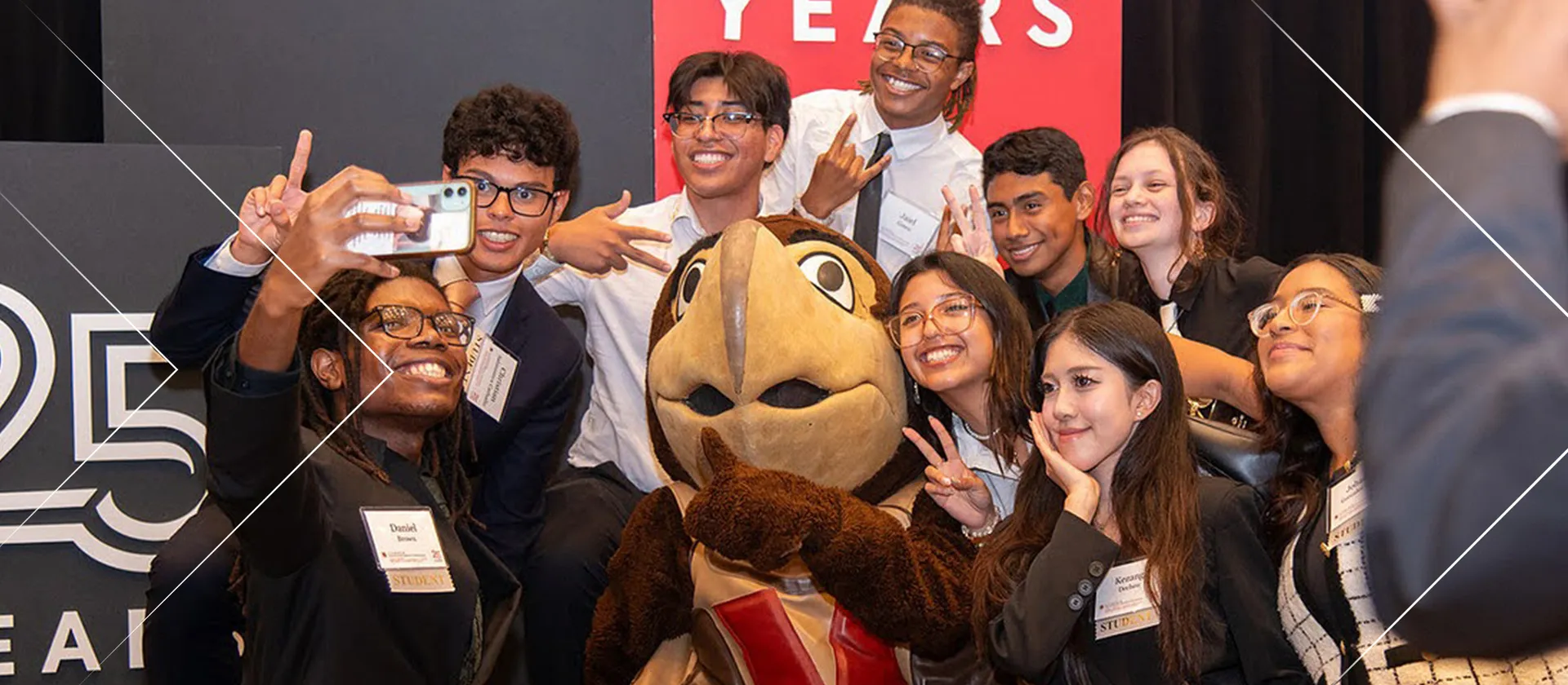 A group of University of Maryland students gather around the school's mascot, a brown terrapin, and take a selfie with a cell phone camera.